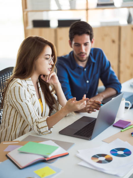 Millennial young woman working with her office partner using a laptop.